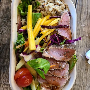 Debutea - Brooklyn - PEPPER TUNA SALAD - A poke bowl featuring sliced tuna, mixed greens, cherry tomato, rice, and vegetables in a white container on a wooden surface. - Poke Near Me - Brooklyn, New York