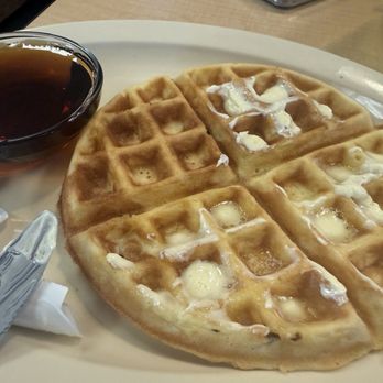 Kettle Restaurant - Waffle - A plate with four waffles topped with butter and syrup, accompanied by a small cup of syrup or tea, on a restaurant table. - Breakfast & Brunch Near Me - Tucson, Arizona