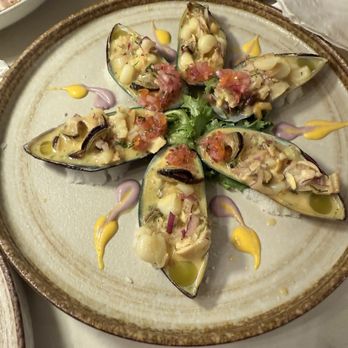 Fusionista - A plate of oysters topped with chopped ingredients, garnished with colorful sauces, and arranged on a bed of greens, served on a ceramic dish. - Peruvian Near Me - Montclair, New Jersey