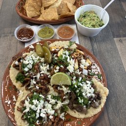 Al pastor, soyrizo, carne asada + chips, guacamole, and salsa in the background Al pastor, soyrizo, carne asada + chips, guacamole, and salsa in the background