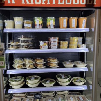 Righteous Kitchen - a display of food in a refrigerator - Refrigerated display case at Righteous Kitchen showcasing salads, sandwiches, and desserts, with a sign reading 'At Righteously' above. - Caterers Near Me - Lombard, Illinois