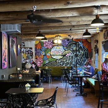 Blackbird Coffee House - A cozy coffee shop features a vibrant mural of a bird and flowers on the back wall, with seating including tables, chairs, and a bench. Customers are working on laptops or reading. - Coffee & Tea Near Me - Albuquerque, New Mexico