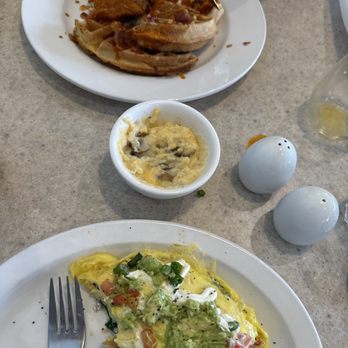 Wild Eggs - The image shows a breakfast meal with an omelet topped with vegetables, a small bowl of mashed potatoes with gravy, and a plate of toast with toppings, on a table. - Breakfast & Brunch Near Me - Avon, Indiana