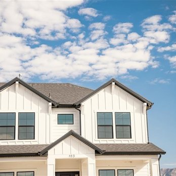 Builders FirstSource - A modern two-story white house with black-framed windows stands against a bright blue sky filled with scattered white clouds.... - Hardware Stores Near Me - Bainbridge Is., Washington
