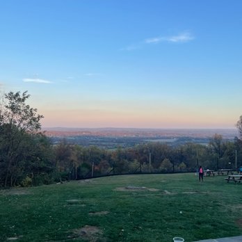 Bear Chase - An outdoor scene featuring a grassy area with trees on the left and right, a few people, and a distant horizon at sunset. - Breweries Near Me - Bluemont, Virginia