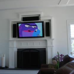 Audio Den - An Elite Plasma hung over a fireplace surrounded by Bowers and Wilkins on wall speakers. Recessed components assure a clean look