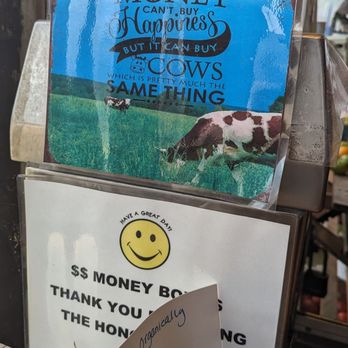 Percy Thomson Meadows - The image shows a sign with a quote about money and happiness, featuring a background of cows grazing in a lush green field. The quote emphasizes that cows are similar to money in that they can be bought but not happiness. The sign is placed on a wooden surface near a window, with additional notes and signs below it, including a handwritten note about organic tomatoes. - Farmers Market Near Me - Bethlehem, Connecticut