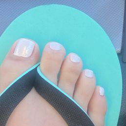 Look how slanted my toe nail is and how my cuticles are still over my nail bed. - The image depicts a person's foot with painted toenails, wearing a flip-flop sandal with a black strap and a turquoise sole. The toenails are painted with a light, possibly white or pale color, and the background appears to be a textured surface, possibly a mat or flooring. The focus is on the toes and the sandal, with clear details of the nail polish and sandal design.