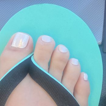 Luxury Nails and Spa - Look how slanted my toe nail is and how my cuticles are still over my nail bed. - The image depicts a person's foot with painted toenails, wearing a flip-flop sandal with a black strap and a turquoise sole. The toenails are painted with a light, possibly white or pale color, and the background appears to be a textured surface, possibly a mat or flooring. The focus is on the toes and the sandal, with clear details of the nail polish and sandal design. - Hair Removal Near Me - Albuquerque, New Mexico
