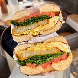 A sandwich featuring fried fish fillet, scrambled eggs, lettuce, and tomato slices on a sandwich bun.