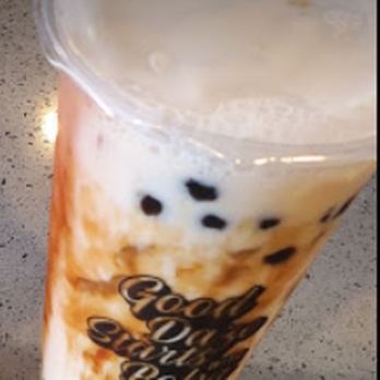 Tea Daze - A clear plastic cup contains bubble tea with black tapioca pearls settled at the bottom. The drink appears to be a milk-based tea with a light, creamy color. The cup has a printed logo that reads 'Good Vibes Only' and is placed on a speckled countertop surface. - Coffee & Tea Near Me - Modesto, California