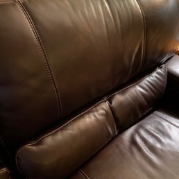 A dark brown leather sofa with visible stitching on the backrest and seat cushion, showing a smooth, shiny surface.