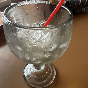 Two Brothers - Empty margarita - A large, clear glass filled with ice and a red straw, placed on a wooden table in a restaurant setting. - Mexican Near Me - Sandy, Oregon