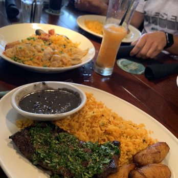 Bahama Breeze - Flank steak with fresh chimichurry, plantains and rice.  The far left plate- seafood paella - Bars Near Me - Troy, Michigan