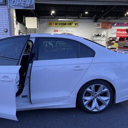 25% 3M ceramic infrared - A white Volkswagen sedan with the front door open is parked outside a window tinting business, with signs and tools visible inside.