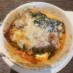 Vegetarian lasagna - A bowl of vegetarian lasagna with melted cheese and spinach, served on a wooden table, with a fork nearby.