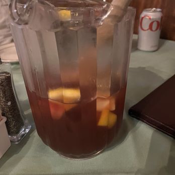 Fernandes steakhouse - A glass pitcher filled with sangria containing fruit pieces and a wooden muddler, placed on a table at a restaurant. - Portuguese Near Me - Newark, New Jersey