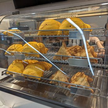 The Dapper Doughnut Cafe - Patties and Samosas - A glass display case contains samosas and patties, arranged on metal racks, at a food business specializing in patties and samosas. - Coffee & Tea Near Me - Toronto, Ontario