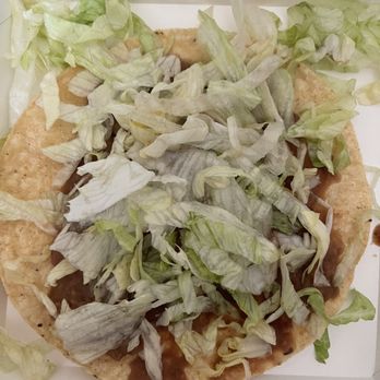 Del Taco - a tortilla with lettuce and onions - A pizza with a thin crust topped with shredded lettuce and other ingredients, placed inside a white takeout box. The lettuce covers most of the pizza surface, and some pieces are spilling over the edges. - Mexican Near Me - Mesa, Arizona