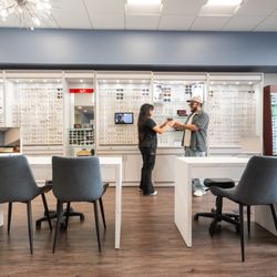 Custom Eyes Optometry - An optician assisting a patient in a modern showroom with numerous eyewear options at Custom Eyes Optometry, Costa Mesa, CA.