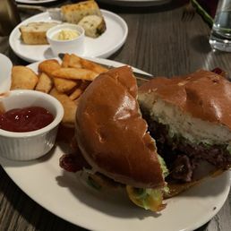 Burger - A burger with a toasted bun, beef patty, lettuce, and other toppings, served with fries, ketchup, and potato wedges at Elsie's Table.