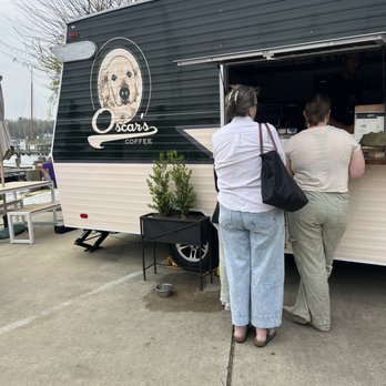 Oscar's Coffee - Two women stand at Oscar's Coffee food truck, which has a logo featuring a dog's face, near a marina with boats and trees. - Coffee & Tea Near Me - Annapolis, Maryland
