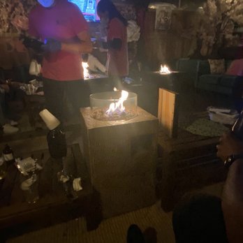 Hook Hall - Fire pits - A person in a pink shirt and face mask stands near a fire pit inside a dimly lit venue, with other people and fire pits visible in the background. - Venues & Event Spaces Near Me - Washington, DC, District of Columbia