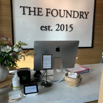 The Foundry - Inside of the store. - Reception area with a computer, flowers, and signage for The Foundry, established in 2015, on a marble counter. - Women's Clothing Near Me - Clovis, California