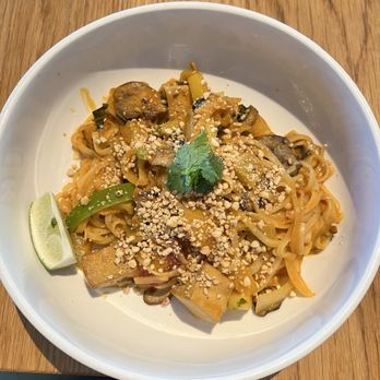 SŌW Plated - Pad Thai - A bowl of pad thai featuring noodles, mushrooms, zucchini, and crushed peanuts, garnished with cilantro and a lime wedge. - New American Near Me - Upper Arlington, Ohio