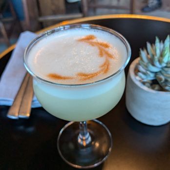 Folklore - Whiskey sour - A pale yellow cocktail with a frothy surface and caramel swirl garnish served in a coupe glass on a dark table at a restaurant or bar. - Vinyl Records Near Me - Napa, California