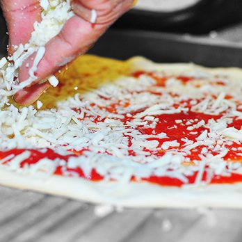 The Pizzeria - a person sprinkling cheese on a pizza - Pizza Near Me - Brownsville, Texas The Pizzeria - a person sprinkling cheese on a pizza - Pizza Near Me - Brownsville, Texas