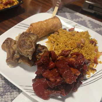 Fortune Cookie - A white plate holds fried rice with diced vegetables and meat, sweet and sour pork, a spring roll, and pork ribs, with a hand holding chopsticks. - Chinese Near Me - Schenectady, New York