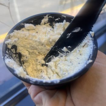 Open Sesame - Everything cream cheese - A black bowl holds a serving of cream cheese mixed with black pepper, with a black butter knife inserted into the mixture. The bowl is being held by a person's hand, and the background shows a window with natural light. - Bagels Near Me - Basalt, Colorado