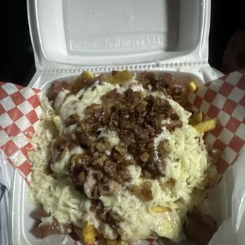 Medallo Spring - A foam takeout container holds cheese fries topped with ground beef, melted cheese, and yellow corn, served with checkered paper lining. - Fast Food Near Me - Spring, Texas