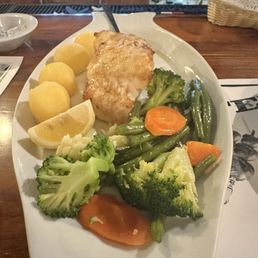 Chilean Sea  Bass - A seafood dish featuring a grilled fish fillet, boiled potatoes, lemon wedges, and steamed broccoli, carrots, and green beans on a white platter.