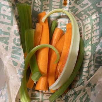 Wingstop - Veggie Sticks - A mix of fresh celery sticks, carrot sticks, and a leek is placed inside a paper bag with printed text. - Chicken Wings Near Me - Mountain View, California
