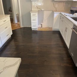 The image shows a kitchen with dark wood flooring, white cabinets, and a partially finished wall area, indicating ongoing renovation.