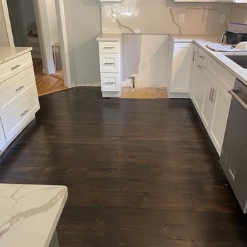 Tan's Floor Service - The image shows a kitchen with dark wood flooring, white cabinets, and a partially finished wall area, indicating ongoing renovation. - Flooring Near Me