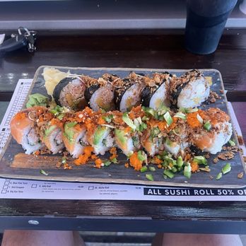 Dragon Sushi - Hawaii roll, Da Bomb roll - A rectangular glass plate holds two rows of sushi rolls with different toppings and ingredients, including fish, avocado, and crunchy garnishes. The plate is on a dark wooden table, with a black drink in a tall cup and a set of keys nearby. The sushi appears freshly prepared, with colorful garnishes and sauces, and the setting suggests a casual dining environment. - Sushi Bars Near Me - Albuquerque, New Mexico
