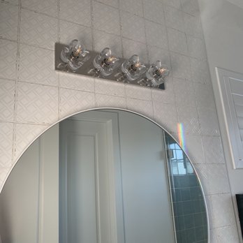 Sun Lighting - Girl's bath - The image shows a section of a bathroom wall with a round mirror, a contemporary light fixture with multiple bulbs, and a rainbow reflection on the tiled surface. The wall tiles have a textured pattern, and there is a window with shutters visible in the reflection. The overall setting appears to be a well-lit bathroom interior. - Lighting Fixtures & Equipment Near Me - Tempe, Arizona