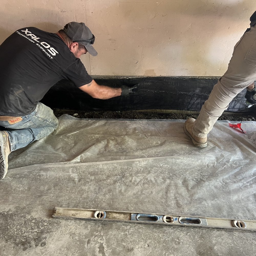 Xalos Foundation Support - Adding carbon fiber strap and epoxy. The carbon fiber runs both above and below grade where they cut out the concrete floor. - Foundation Repair Near Me Xalos Foundation Support - Adding carbon fiber strap and epoxy. The carbon fiber runs both above and below grade where they cut out the concrete floor. - Foundation Repair Near Me