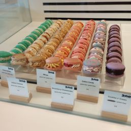 Macarons - Assorted macarons in various colors and flavors are arranged in a bakery display case, with labels indicating flavors and prices.