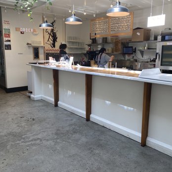 Forward Brewing - A cafe or restaurant interior with a white counter, two staff members preparing food or drinks, and hanging pendant lights. The space has a clean, minimalist design with natural light. - Brewpubs Near Me - Annapolis, Maryland