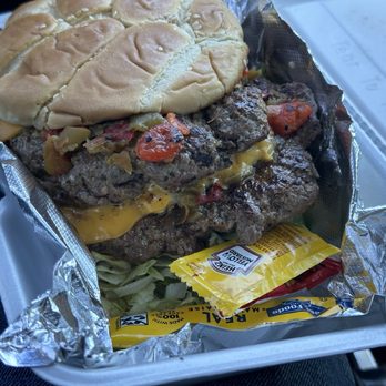 Blue Line Grill - Another picture of this beautiful burger! - A double beef burger with melted cheese, vegetables, and a sandwich bun, served in a foil-lined takeout container with condiments. - Food Trucks Near Me - Belen, New Mexico