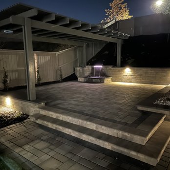 Reliable Landscaping And Design - Raised platform area with pergola at night. Lit waterfall and capstones set a relaxing backyard retreat feel. - Landscaping Near Me - Orangevale, California Reliable Landscaping And Design - Raised platform area with pergola at night. Lit waterfall and capstones set a relaxing backyard retreat feel. - Landscaping Near Me - Orangevale, California