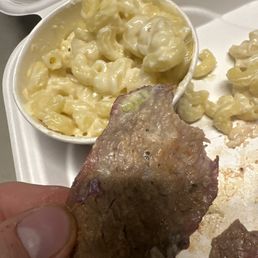 a hand holding a piece of meat and macaroni and cheese