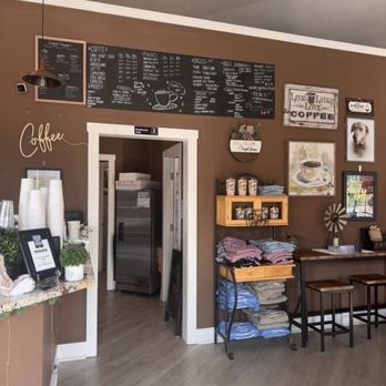 Corner Grounds Cafe  - The image shows the inside of a coffee shop with a brown wall, a chalkboard menu, wall art, and a merchandise shelf with folded clothing. - Coffee & Tea Near Me - Odessa, Delaware