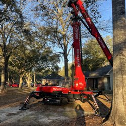 Singletary's Tree Service - A red hybrid spider lift is set up on a residential property among large trees. The lift is in a partially raised position and appears ready