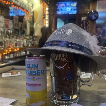 Olde Towne Tavern - Won a beer mug, t-shirt, hat and a free drink just by participating. - A bar scene featuring a Samuel Adams beer mug topped with a wide-brimmed hat, alongside a can of Sun Ruiser lemonade vodka, on a wooden bar table. - Burgers Near Me - Frederick, Maryland
