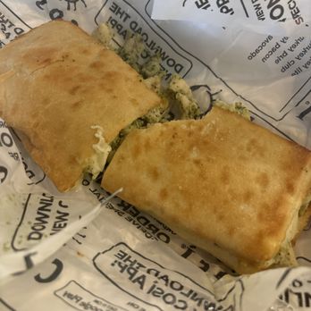 Cosi - Pesto Chicken Melt - Whole - A sandwich with toasted, golden-brown bread is shown, with visible filling of blue cheese and possibly chicken or other ingredients. The sandwich is placed on branded paper with text and graphics, indicating it is from a restaurant or sandwich shop. - Sandwiches Near Me - Baltimore, Maryland